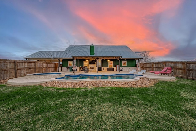 back house at dusk featuring a lawn, a pool with hot tub, and a patio area