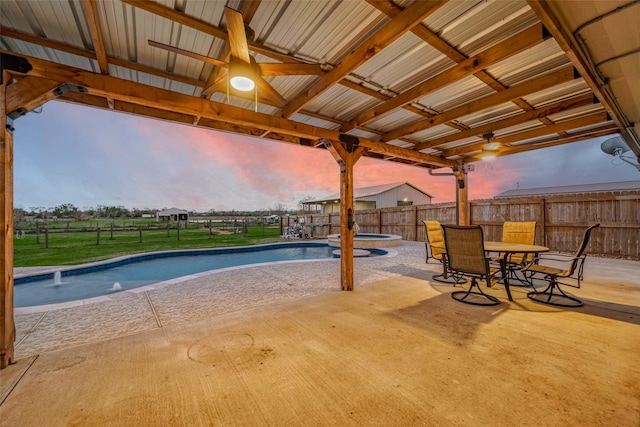 pool at dusk with ceiling fan, an in ground hot tub, and a patio