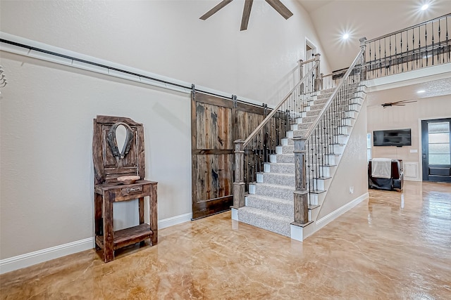 staircase with a barn door, ceiling fan, and a towering ceiling