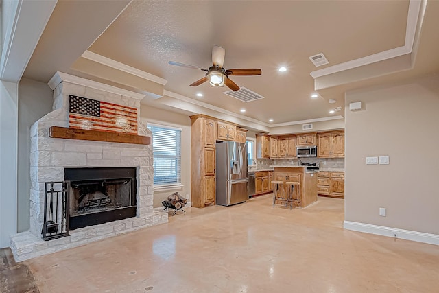 kitchen with ceiling fan, a fireplace, appliances with stainless steel finishes, a kitchen island, and a breakfast bar area