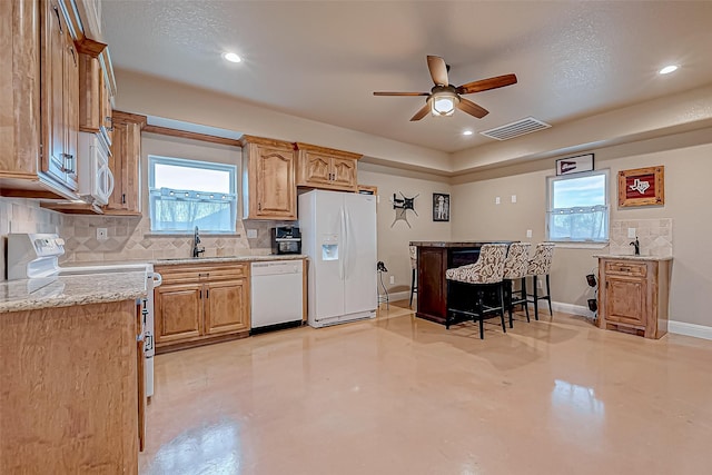 kitchen with light stone countertops, white appliances, a wealth of natural light, and sink