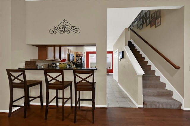 kitchen featuring a breakfast bar, refrigerator, light tile patterned floors, tasteful backsplash, and kitchen peninsula