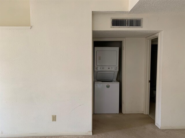 laundry area featuring a textured ceiling, light colored carpet, and stacked washer / drying machine