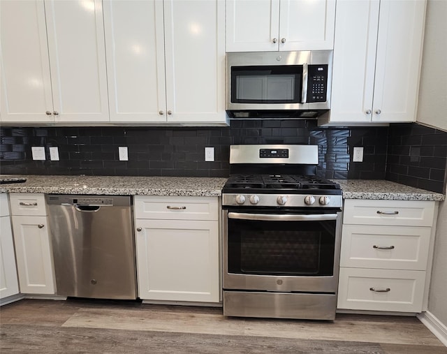 kitchen featuring white cabinets, appliances with stainless steel finishes, light hardwood / wood-style floors, and decorative backsplash