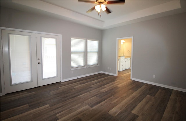 empty room with ceiling fan, dark hardwood / wood-style flooring, a tray ceiling, and french doors