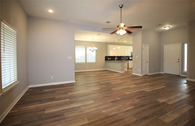 unfurnished living room featuring sink, dark wood-type flooring, and ceiling fan with notable chandelier