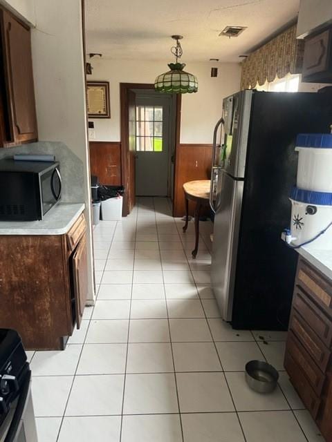 kitchen with wood walls, light tile patterned flooring, and stainless steel refrigerator