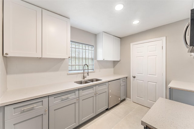 kitchen with light stone counters, stainless steel dishwasher, sink, white cabinetry, and light tile patterned flooring