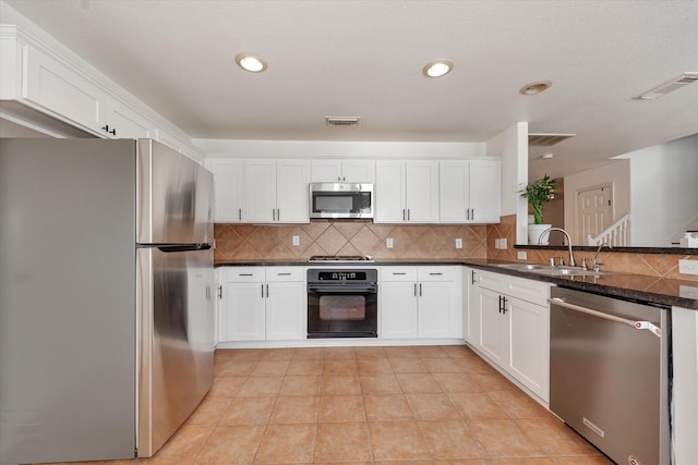 kitchen with white cabinetry, stainless steel appliances, sink, and dark stone countertops