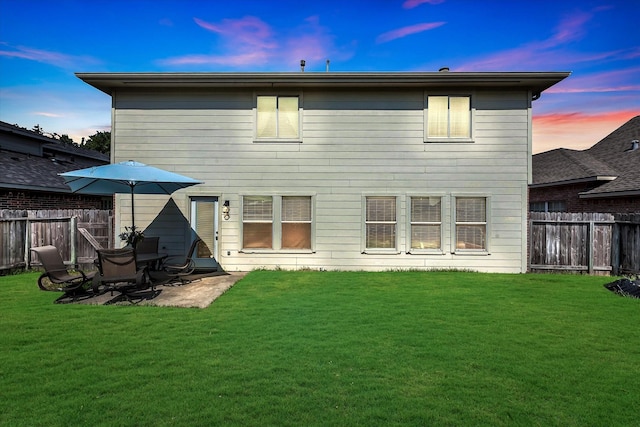 back house at dusk with a yard and a patio