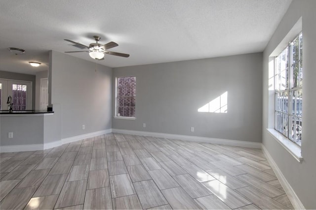 empty room with ceiling fan, a healthy amount of sunlight, sink, and a textured ceiling