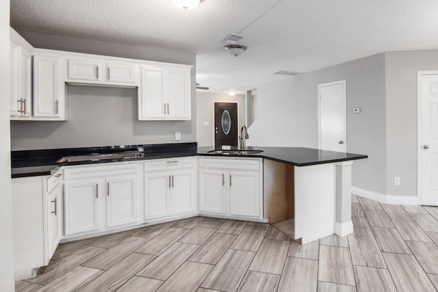 kitchen featuring sink, white cabinetry, a textured ceiling, gas cooktop, and kitchen peninsula