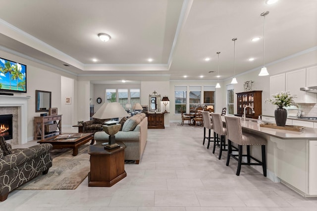 living room with a raised ceiling, crown molding, and sink