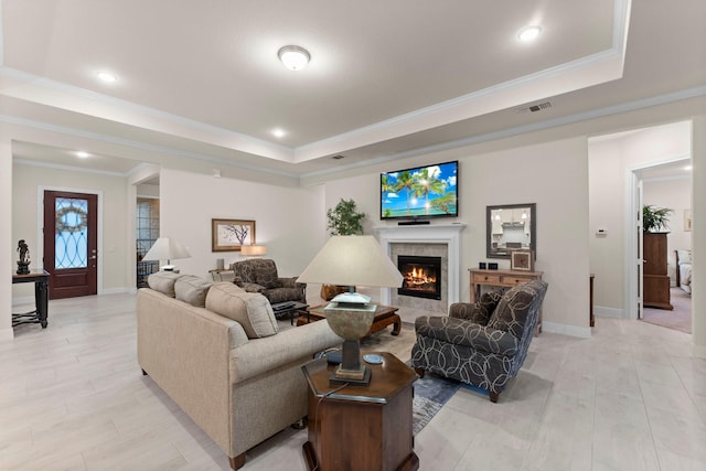 living room featuring a tile fireplace, a tray ceiling, and ornamental molding