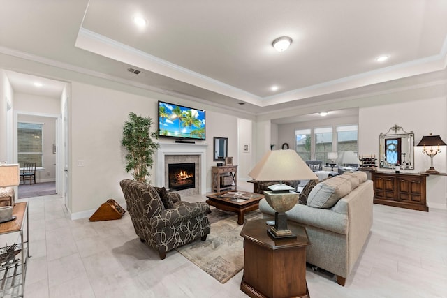 living room with ornamental molding, a tray ceiling, and a tiled fireplace