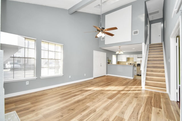 unfurnished living room with ceiling fan with notable chandelier, light hardwood / wood-style floors, beam ceiling, and a high ceiling