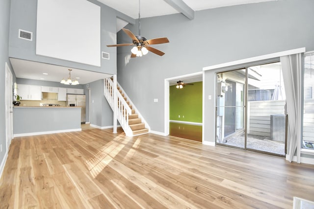 unfurnished living room with a high ceiling, ceiling fan with notable chandelier, light hardwood / wood-style floors, and beam ceiling