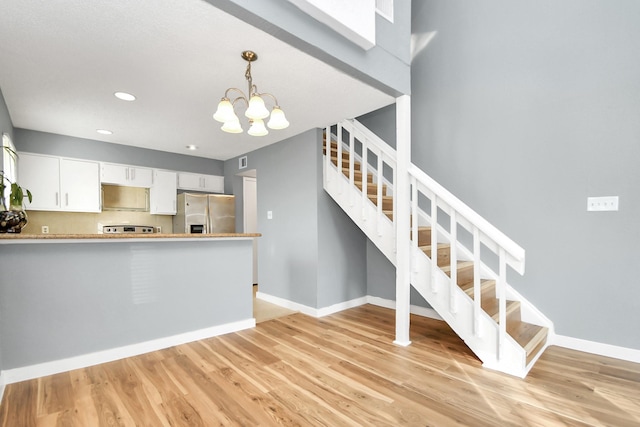 kitchen featuring white cabinets, stainless steel refrigerator with ice dispenser, light wood-type flooring, decorative light fixtures, and a chandelier