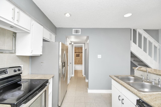 kitchen with sink, light tile patterned floors, a textured ceiling, electric stove, and white cabinets