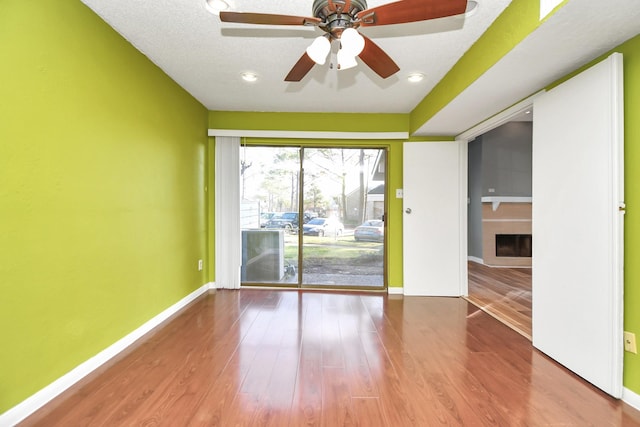 spare room featuring hardwood / wood-style flooring, ceiling fan, a fireplace, and a textured ceiling