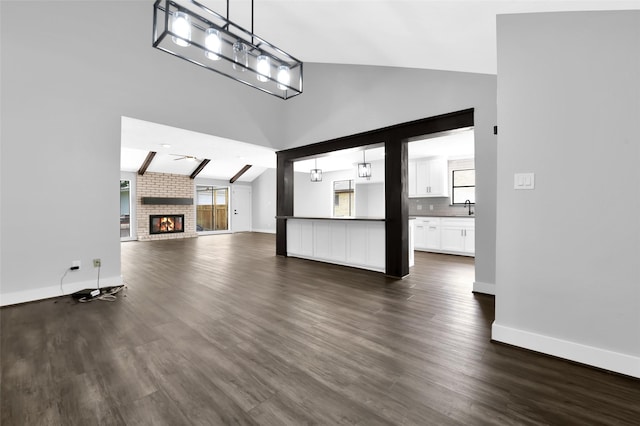 unfurnished living room featuring dark hardwood / wood-style flooring, a brick fireplace, sink, high vaulted ceiling, and beamed ceiling