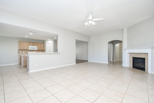 unfurnished living room with a tiled fireplace, ceiling fan, and light tile patterned floors