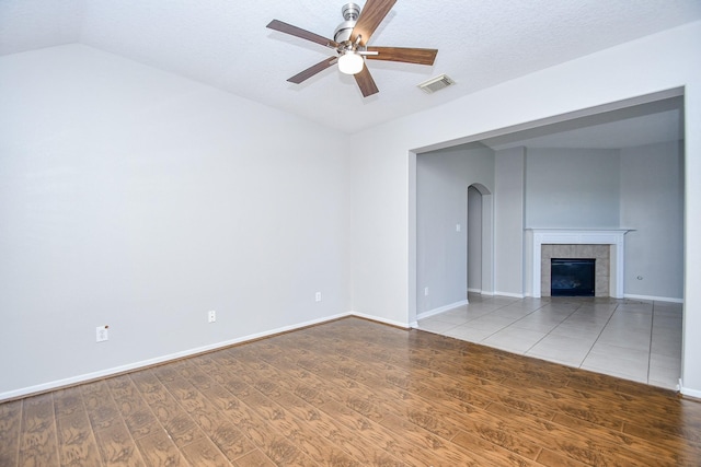 unfurnished living room with a textured ceiling, lofted ceiling, a tiled fireplace, hardwood / wood-style floors, and ceiling fan