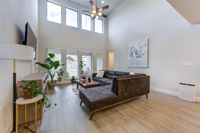 living room featuring ceiling fan, a high ceiling, and light wood-type flooring