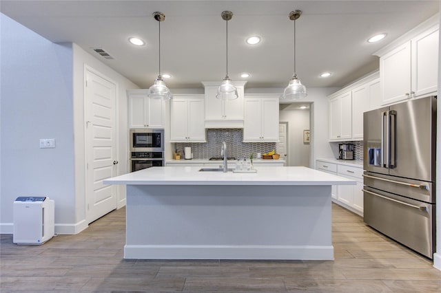 kitchen featuring backsplash, an island with sink, decorative light fixtures, white cabinets, and appliances with stainless steel finishes