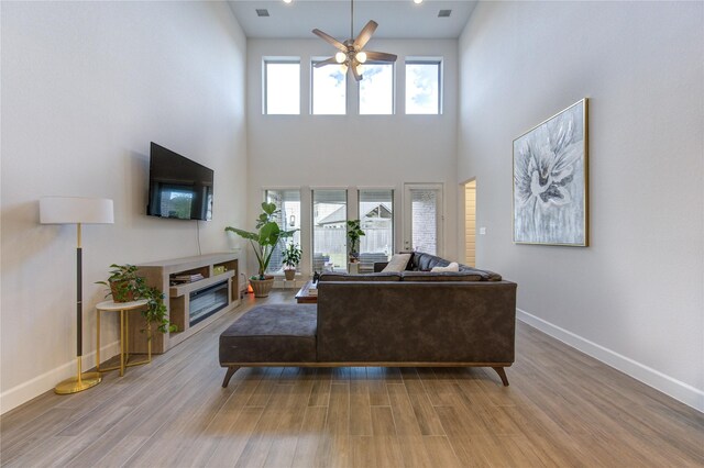 living room featuring ceiling fan, light wood-type flooring, and a towering ceiling