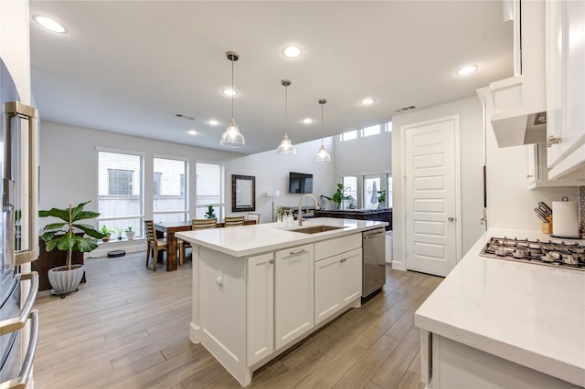 kitchen with stainless steel appliances, a kitchen island with sink, sink, pendant lighting, and white cabinetry