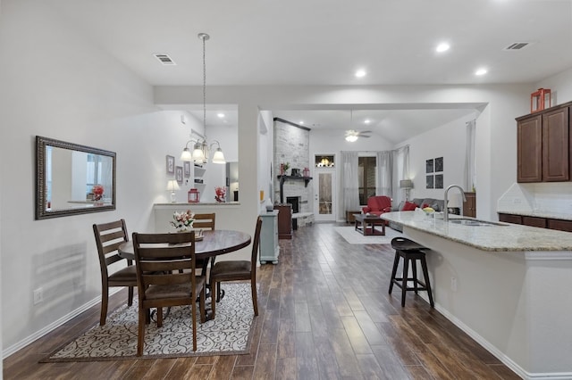 dining area featuring a large fireplace, sink, and ceiling fan with notable chandelier