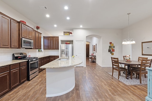 kitchen with appliances with stainless steel finishes, tasteful backsplash, a kitchen island with sink, pendant lighting, and a notable chandelier