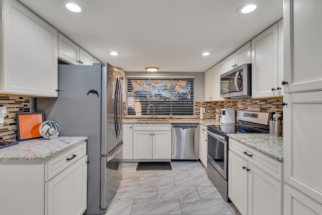 kitchen featuring white cabinets, appliances with stainless steel finishes, decorative backsplash, and light stone countertops