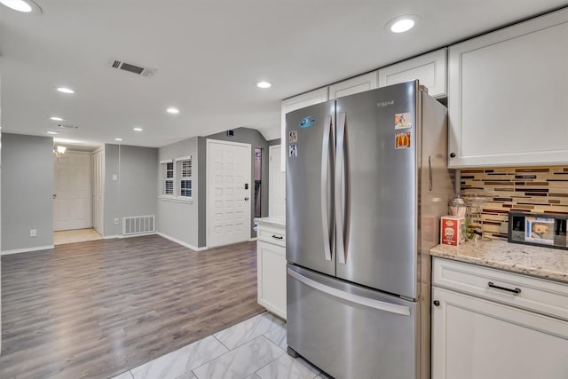 kitchen with white cabinets, stainless steel fridge, light stone counters, and tasteful backsplash