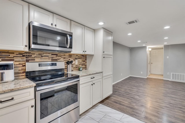 kitchen with light stone countertops, appliances with stainless steel finishes, backsplash, and white cabinetry