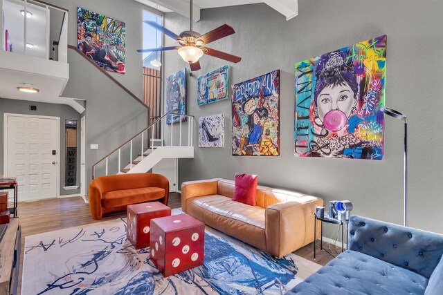 living room with beamed ceiling, a high ceiling, light hardwood / wood-style floors, and ceiling fan