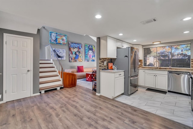 kitchen with sink, backsplash, appliances with stainless steel finishes, white cabinets, and light wood-type flooring