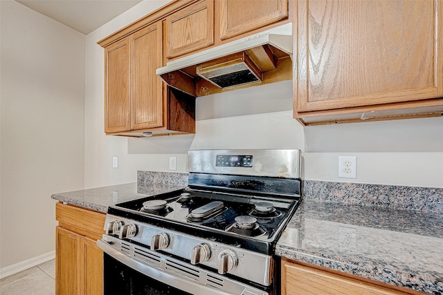 kitchen featuring gas stove, dark stone countertops, and light tile patterned flooring