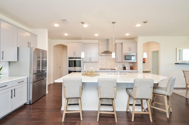 kitchen with pendant lighting, a center island with sink, wall chimney exhaust hood, decorative backsplash, and stainless steel appliances