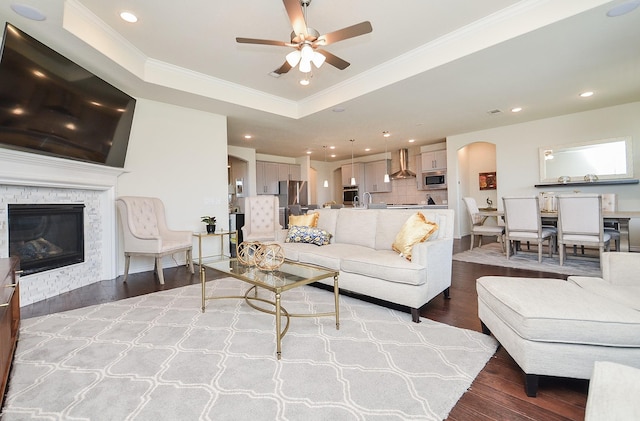 living room featuring a raised ceiling, ceiling fan, crown molding, wood-type flooring, and a fireplace