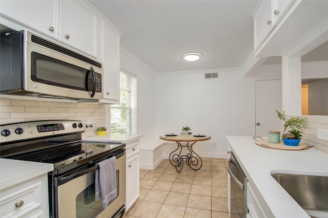 kitchen featuring light tile patterned flooring, appliances with stainless steel finishes, white cabinets, backsplash, and ornamental molding