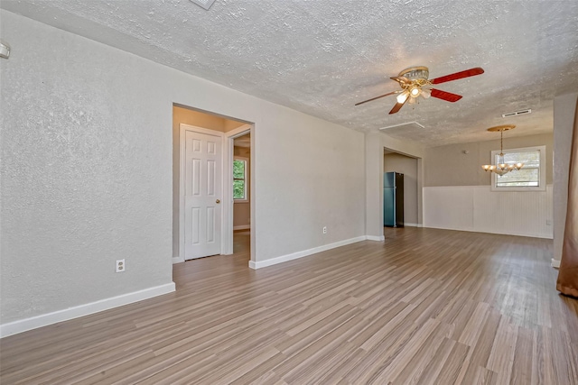 empty room with a textured ceiling, ceiling fan with notable chandelier, and light hardwood / wood-style flooring