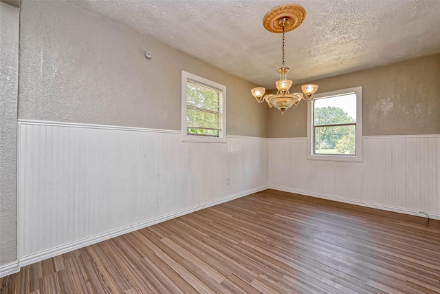 empty room with a chandelier, wood-type flooring, and a wealth of natural light