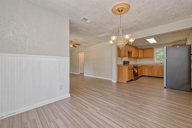 kitchen featuring black electric range oven, stainless steel fridge, light hardwood / wood-style floors, decorative light fixtures, and ceiling fan with notable chandelier