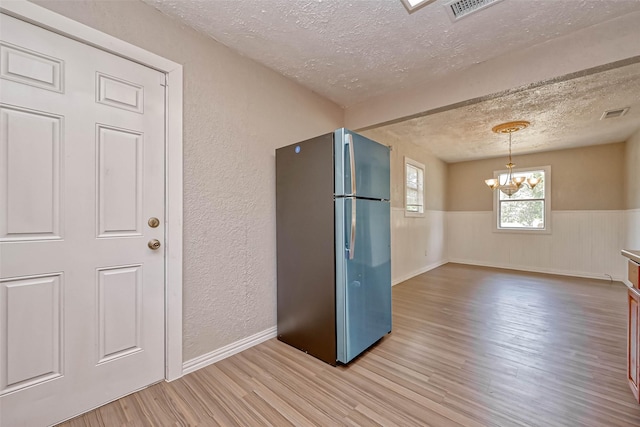 kitchen featuring hanging light fixtures, light hardwood / wood-style flooring, a notable chandelier, stainless steel fridge, and a textured ceiling