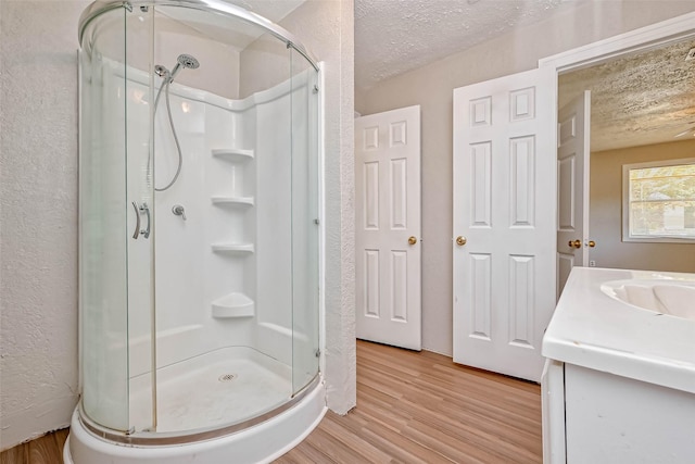 bathroom featuring hardwood / wood-style floors, vanity, a shower with shower door, and a textured ceiling