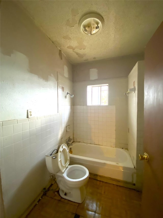 bathroom with a textured ceiling, tile walls, tiled shower / bath combo, and toilet