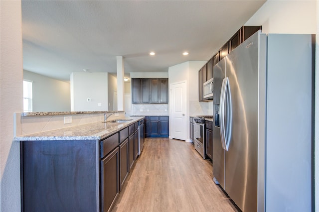 kitchen featuring appliances with stainless steel finishes, backsplash, light stone counters, dark brown cabinetry, and light hardwood / wood-style floors