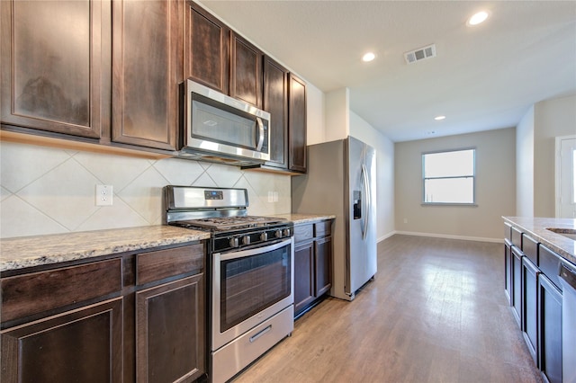 kitchen featuring light stone countertops, appliances with stainless steel finishes, dark brown cabinetry, and light hardwood / wood-style floors